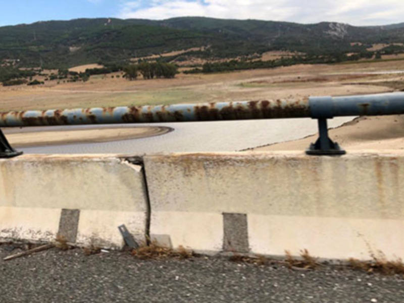 Vista de un puente sobre un río seco, con montañas al fondo y una barrera de seguridad en primer plano.