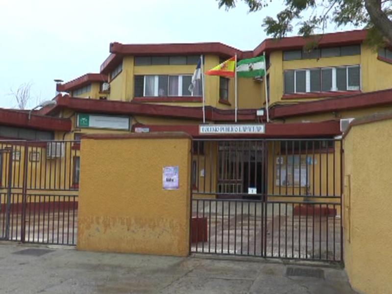 Edificio amarillo con banderas en la parte superior y puerta metálica en el frente.