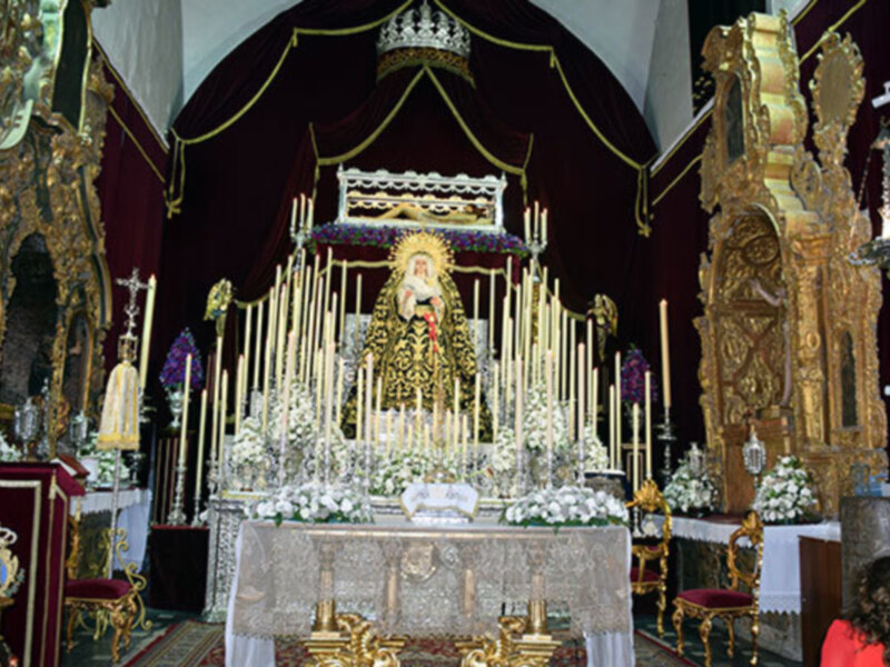 Imagen de una iglesia con altares dorados, velas y flores blancas. La imagen muestra la belleza y la solemnidad de un lugar de culto religioso.