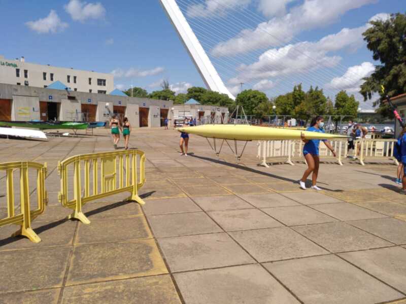 Atletas transportando una canoa en un entorno deportivo junto al puente La Cartuja.