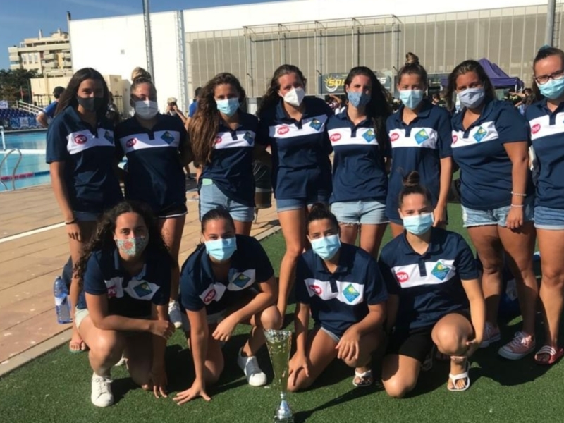 Equipo femenino de natación posando en la piscina, todos con máscaras médicas, vestidos con camisetas y shorts azules con logos de la institución deportiva.