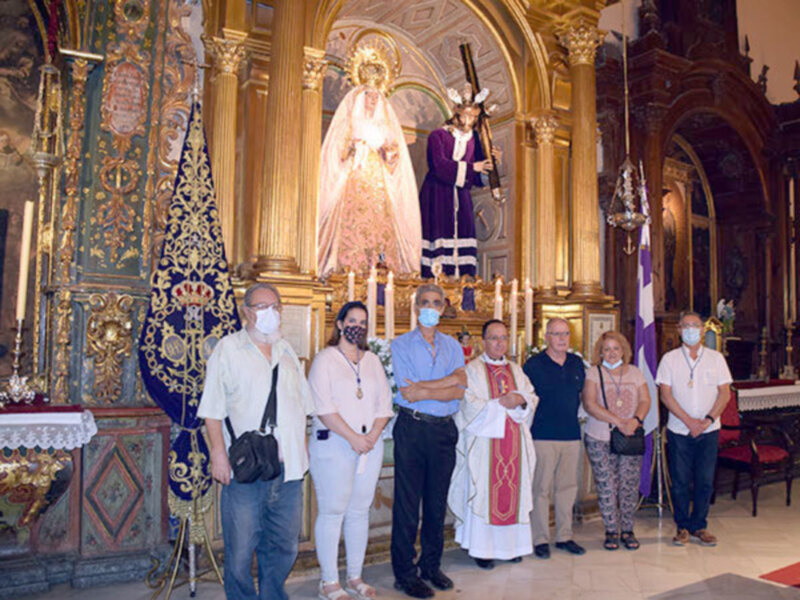 Celebración religiosa en un templo con una imagen de la Virgen y un sacerdote junto a un grupo de personas.