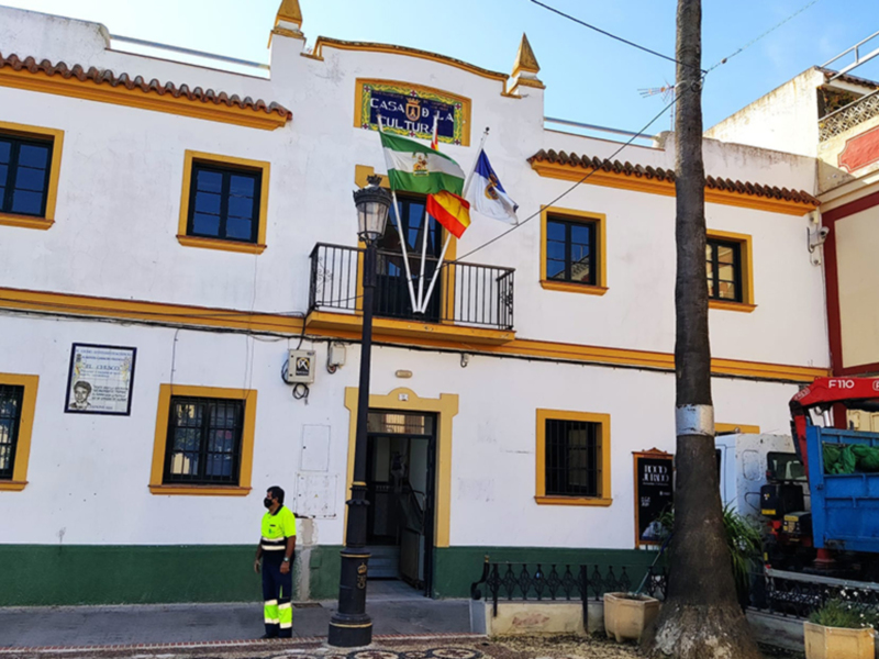 Fachada de la Casa de la Cultura de Sevilla, con banderas y un camión de limpieza en el frente.