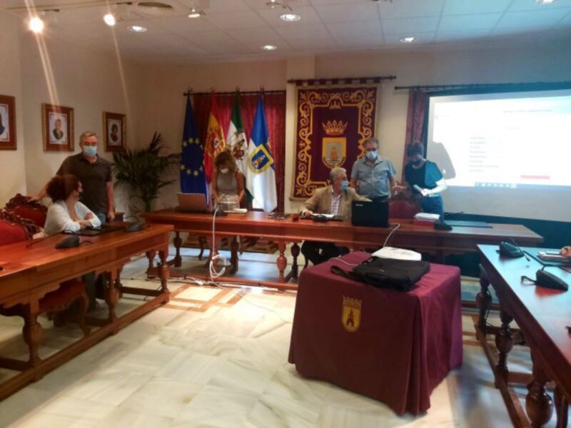 Reunión en una sala oficial con banderas y proyección de presentación en pantalla.