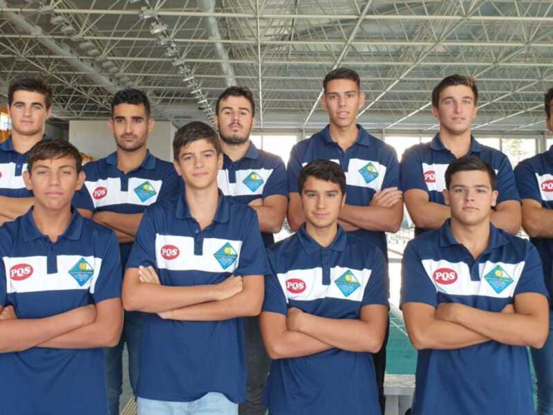 Equipo de jóvenes atletas en uniforme azul con logo PQS, posando con brazos cruzados en un estadio cubierto.