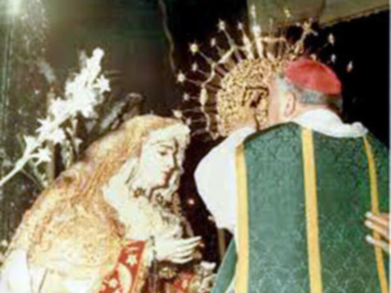 Un sacerdote bendice a una imagen religiosa durante una ceremonia en un entorno festivo con decoraciones navideñas.