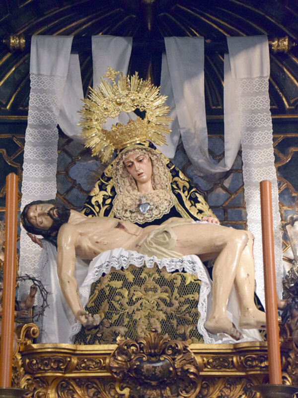 Sagrada representación de la Virgen de la Soledad con el Cristo muerto en su regazo, adorada en un altar ornamental y dorado.