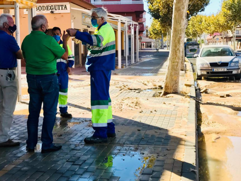 Trabajadores discuten sobre reparación de una fuga de agua en la acera de una calle urbana.