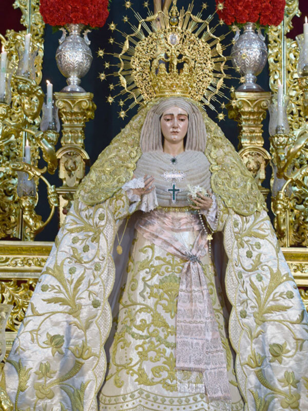 Imagen de la Virgen de la Amargura en su trono ornado con detalles dorados y flores rojas.