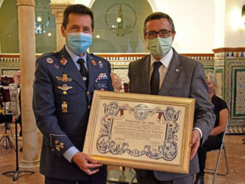 Celebración de un reconocimiento con certificado en un ambiente formal, con presencia de músicos y decoración ornamental.
