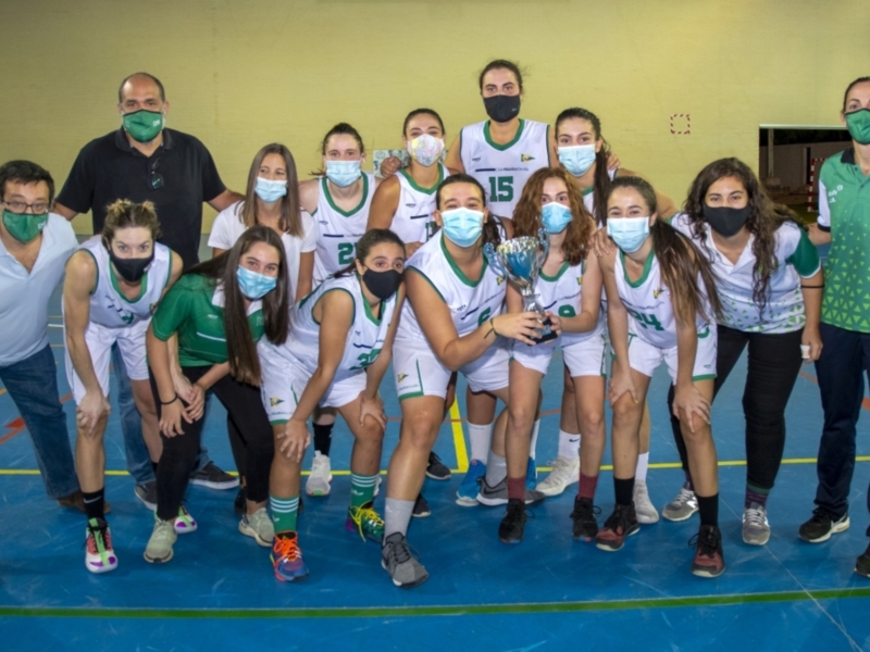 Equipo femenino de baloncesto celebrando con el trofeo en una cancha deportiva.