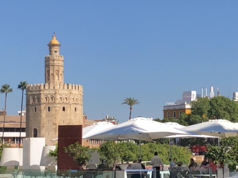 Torre del Oro, Sevilla, España, con terraza de restaurantes en primer plano y palmeras en el fondo.