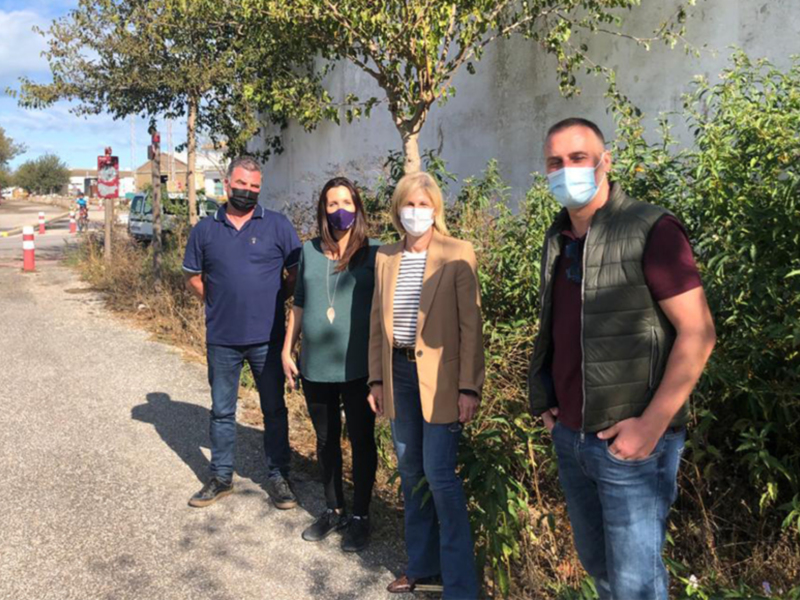 Equipo de trabajo con mascarillas posando al aire libre junto a un camino y arbustos.
