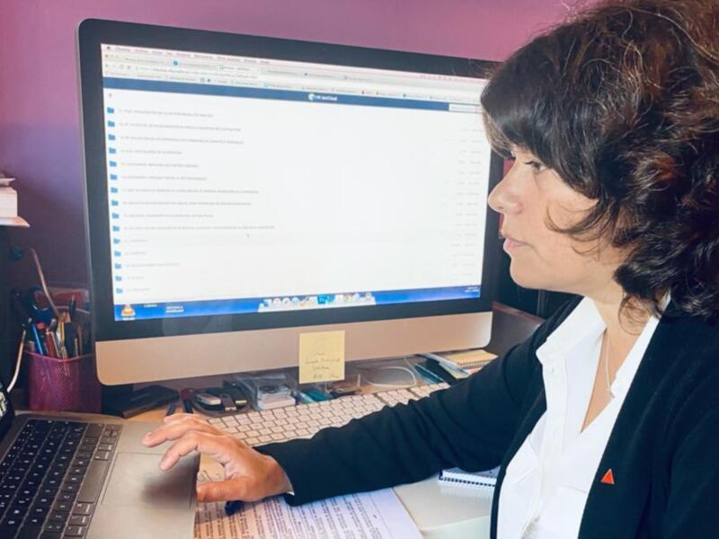Persona trabajando en un escritorio con un monitor de computadora y un portátil, en un ambiente de oficina.