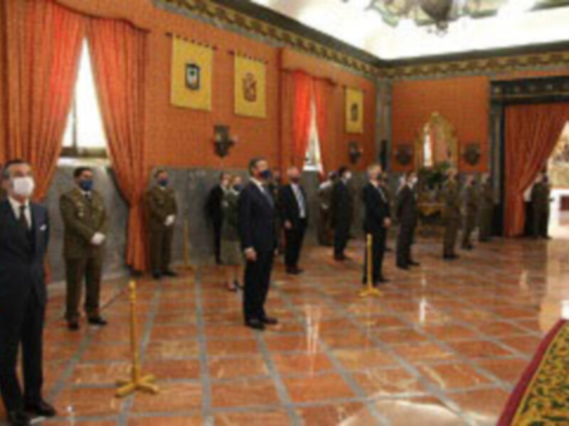 Oficiales militares en una ceremonia formal en un salón decorado con tapices y banderas.