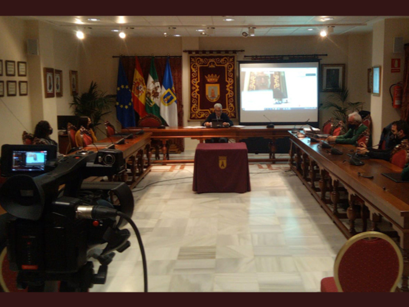 Sala de conferencias con una pantalla proyectora en el centro y dos banderas en el fondo.