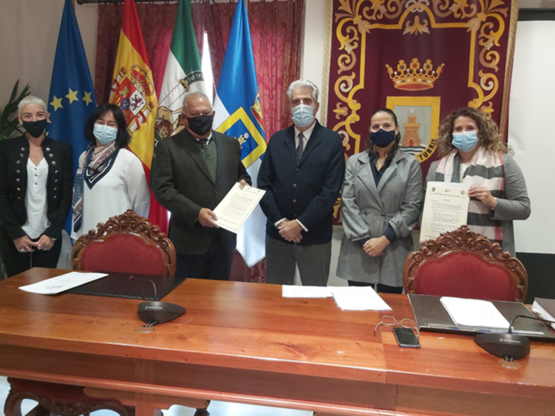 Conferencia de prensa con autoridades locales y representantes de instituciones, con documentos y banderas en el fondo.