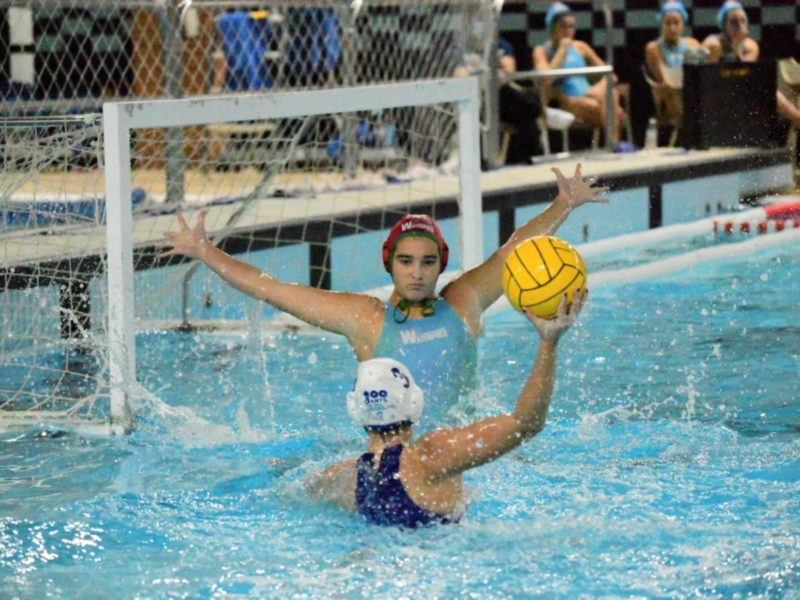 Jugadora de waterpolo en acción, protegiendo el arco durante un partido.