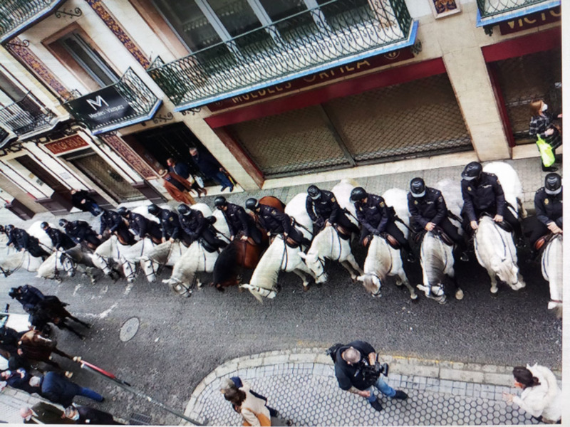 Un grupo de policías montados en caballos patrullan una calle urbana.