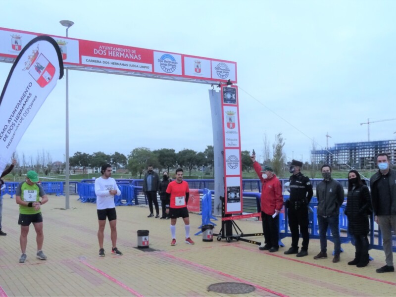 A corredores en una carrera, con un marco de inicio y finalización en el fondo. El evento se llama "Carrera de los Hermanos" y está organizado por la ciudad de Bochum. La carrera parece ser una competencia deportiva importante, con corredores listos para comenzar la carrera.