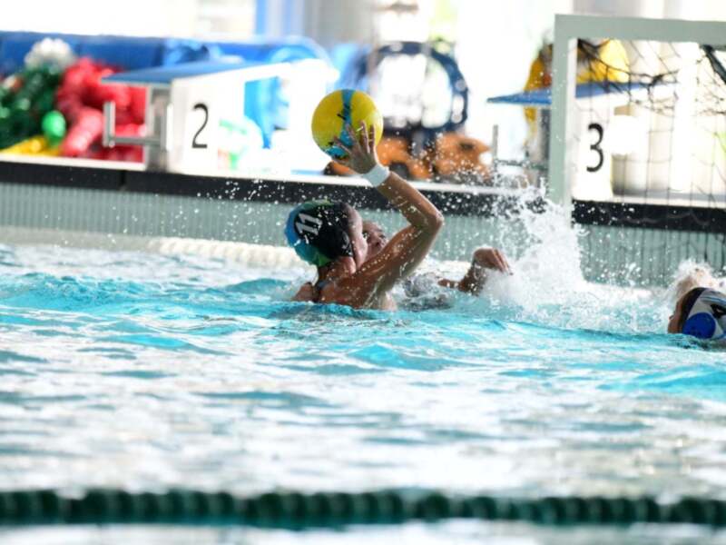 Jugadores de waterpolo compiten por el balón en un partido intenso en una piscina cubierta.