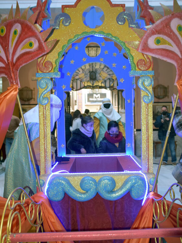 Carroza festiva con decoración brillante y figuras humanas en un evento público.