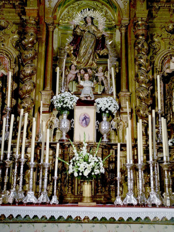 Altar con estatua de Virgen María y adornos florales y candelabros.
