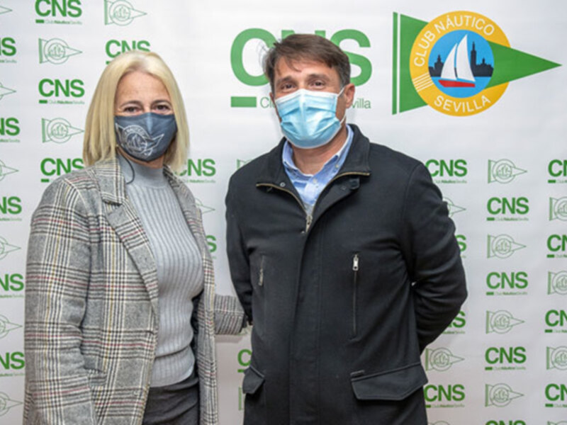 Dos personas posan frente a un fondo con el logo del Club Náutico Sevilla, ambos están usando mascarillas.