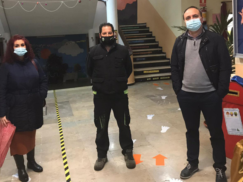 Tres personas con mascarillas en un espacio decorado con motivos navideños, posando en fila.