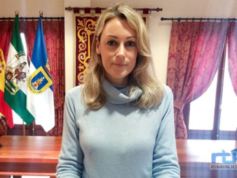 Persona en una oficina municipal con banderas española y andaluza en el fondo.