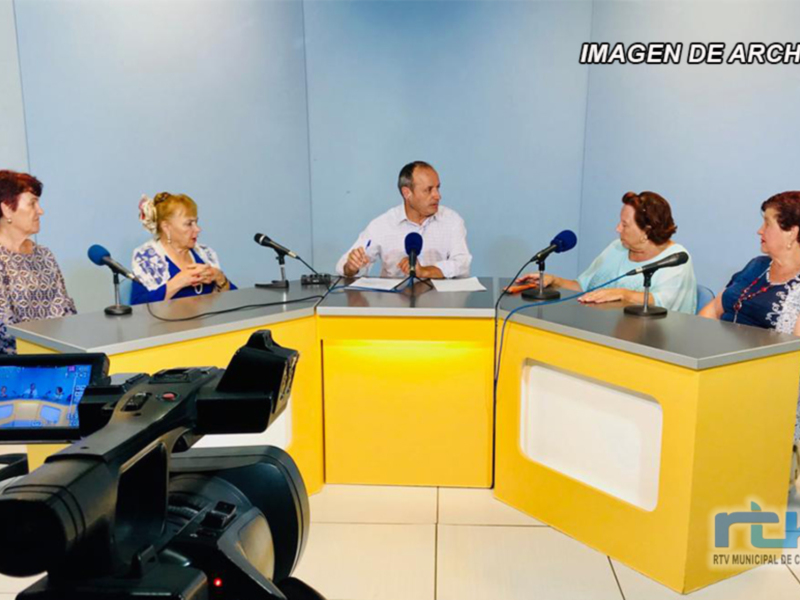 Una conferencia de prensa en un entorno profesional con cuatro personas sentadas frente a micrófonos y un monitor de video.