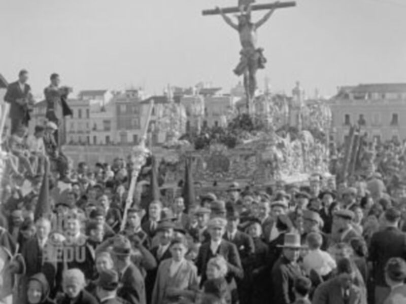 Procesión histórica con una figura de Cristo en la cruz, rodeada por una multitud en una plaza urbana.