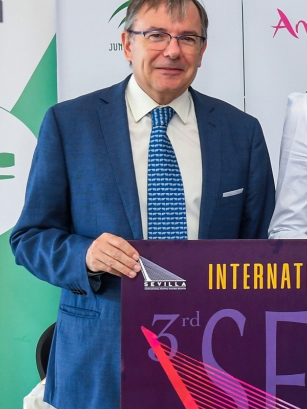 Persona en traje con cartel de '3rd Sevilla International Rowing Masters Regatta'.