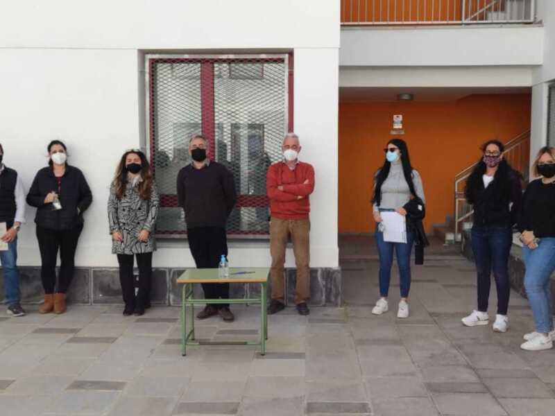 Equipo de profesores y administrativos en una reunión en el patio de un edificio escolar.