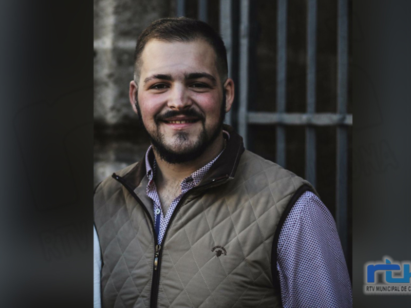 Retrato de hombre sonriente con chaqueta verde y camisa a cuadros, fondo urbano.