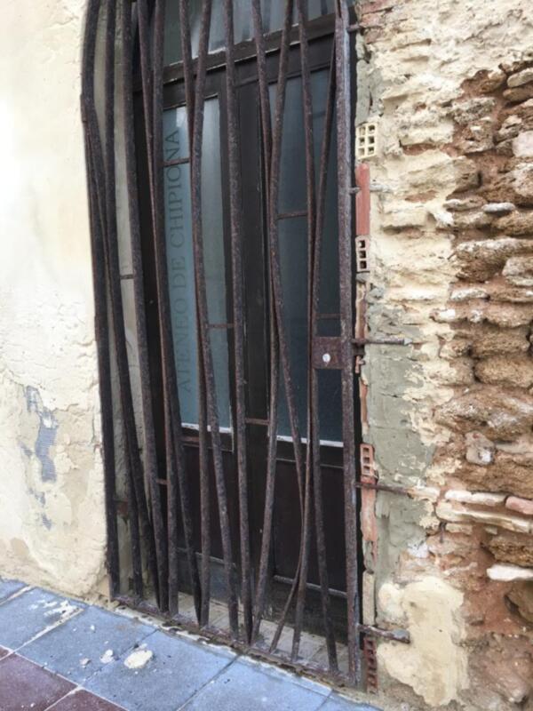 Puerta de metal con rejas en una pared de ladrillo rojo, con el nombre 'ATIENEO DE CHIPIONA' en la parte superior de la puerta.