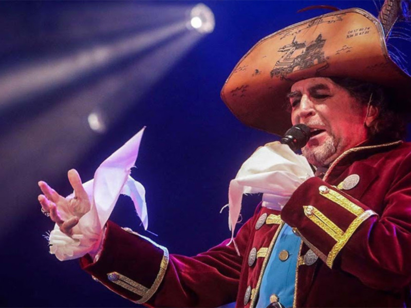 Cantante en traje de capitán pirata, actuando en escenario con iluminación dramática.
