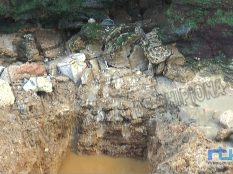 Restos arqueológicos en una excavación costera, con rocas y restos de estructuras antiguas.