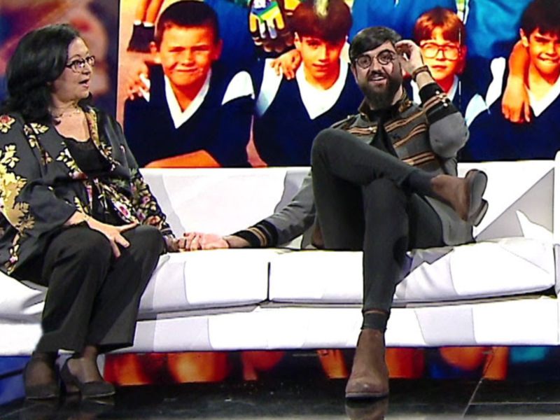 Entrevista en vivo con dos personas sentadas en un sofá blanco, fondo con imágenes de jóvenes en uniforme escolar.