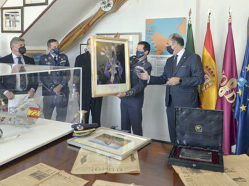 Presentación de un cuadro en un evento oficial con banderas y documentos históricos en el fondo.