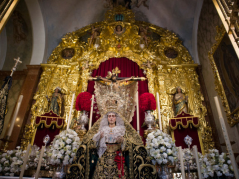 Altar con imagen religiosa en trono dorado, adornado con flores y velas, en un interior de iglesia.