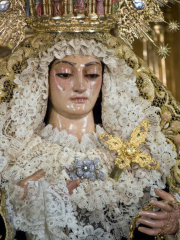 Imagen detallada de una imagen religiosa con vestimentas bordadas y joyas, representando a la Virgen María.