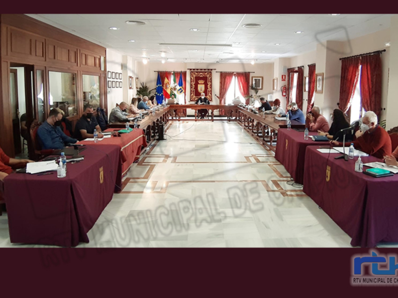 Reunión del Ayuntamiento de Chipiona en una sala con mesas y sillas, donde los asistentes discuten y toman notas.