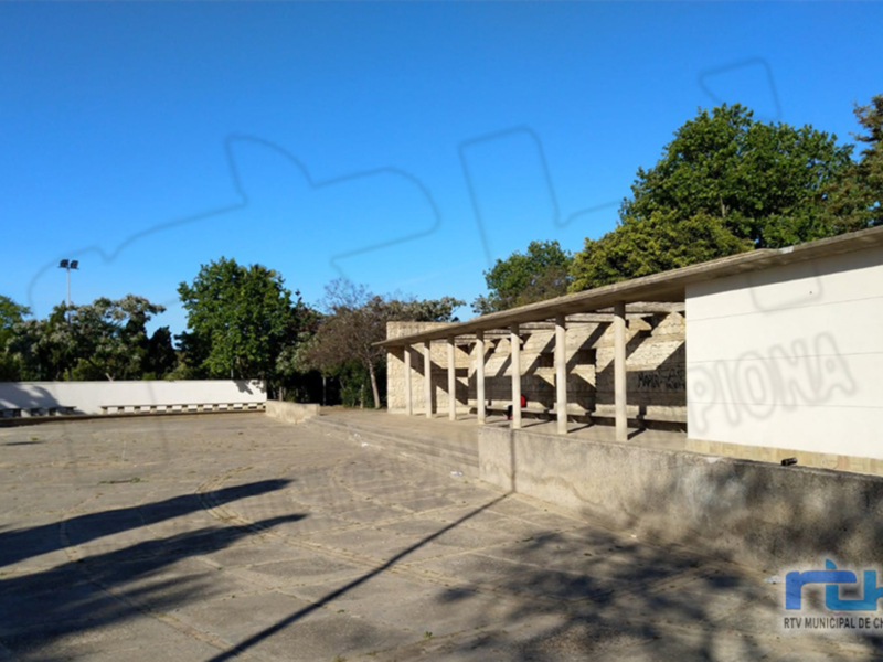Área exterior con bancos y techumbre, rodeada de árboles y un cielo despejado.