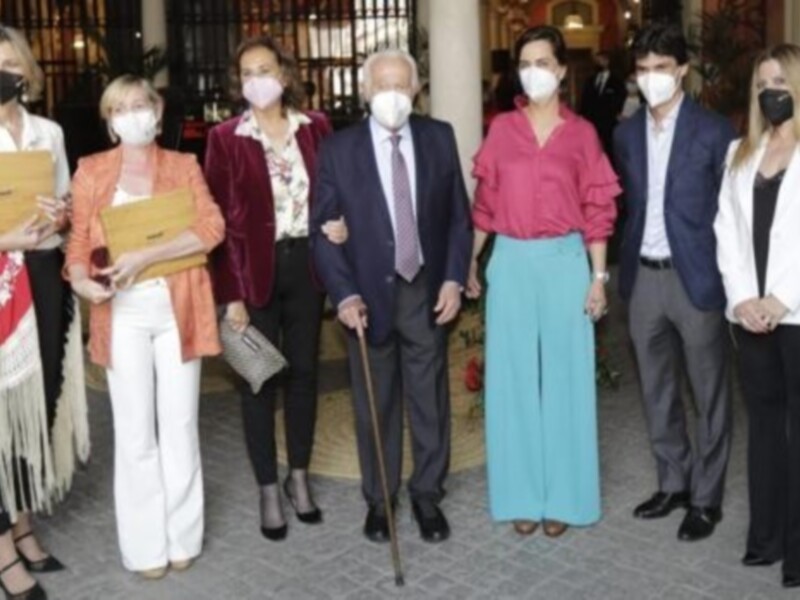 Gruppo di persone in posa con mascherine, indossando abiti formali e colorati, in un ambiente all'aperto.
