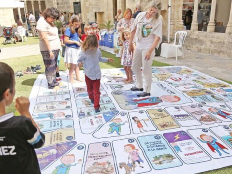 Niños jugando con un gran mapa interactivo en un evento público, mostrando actividades y consejos para la educación y el bienestar de los niños.