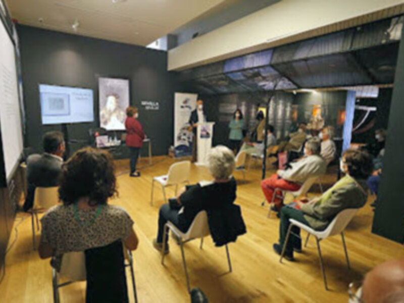 Reunión de discusión en una sala de conferencias con asistentes sentados en sillas y un presentador en el centro.