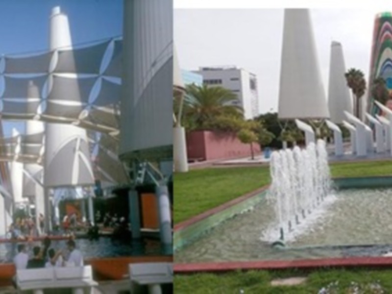 Fuentes y estructuras modernas en un parque público, con un cielo azul y edificios blancos en el fondo.