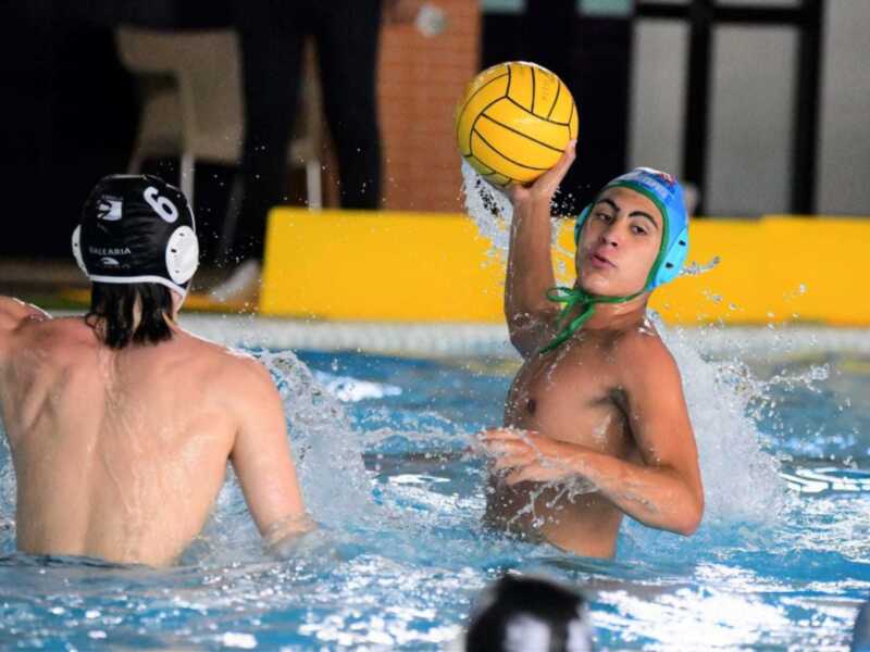 Jugadores de waterpolo en acción durante un partido, uno lanza el balón mientras el otro se prepara para interceptarlo en una piscina.