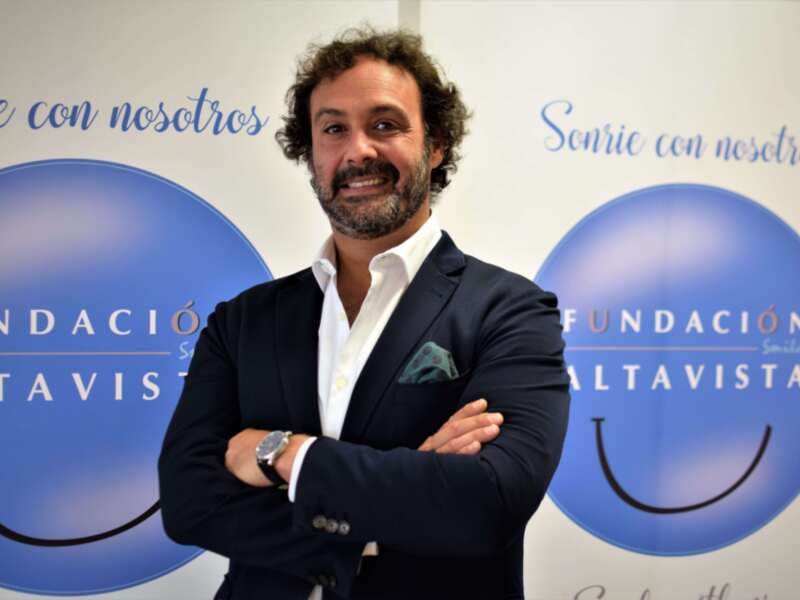 Persona sonriente en traje, fondo con logotipo de Fundación Altavista.
